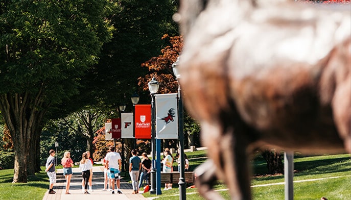 Students walking on sidewalk in quad at Fairfield University on bright sunny day.