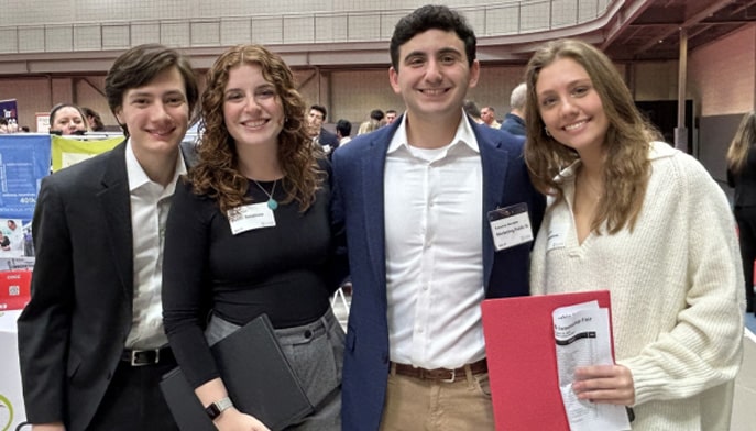 Four students standing in a row looking at camera and smiling at previous career fair.