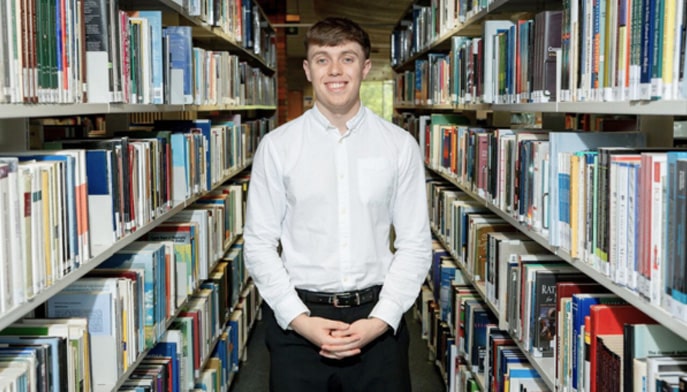 Graduate of the University of Limerick, Conlisk Scholar Evan Mansfield standing in an aisle between bookcases on left and right of him.