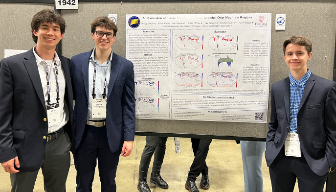 Three male. students stand adjacent to a poster that illustrates a diagram, collaborating and analyzing the details together.