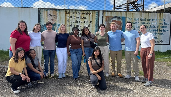 Fairfield students taking a group photo in front of a border fence with inspirational quotes painted on the walls.