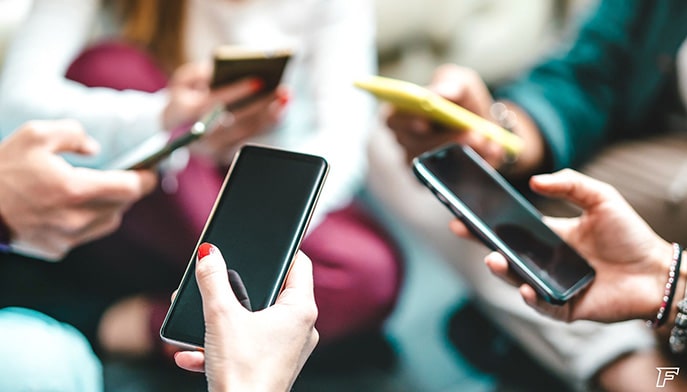 Group of teens sitting in a circle while scrolling on their mobile phones.