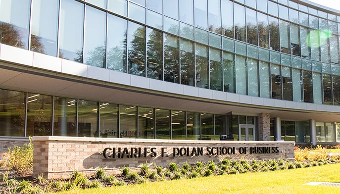 Exterior shot of the modern glass-facade building and brick sign of the Dolan School of Business.