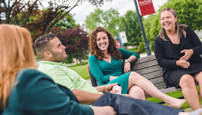 Students on Fairfield University's campus sitting on benches and talking to each other.