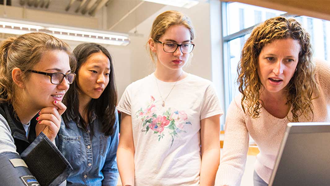 Engineering students standing next to their professor as they show him something on a small portable device. 