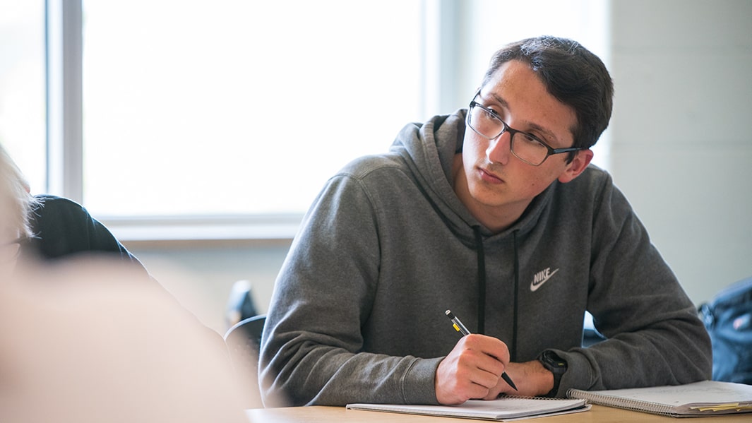 A student writes with a pencil in a notebook at a desk.