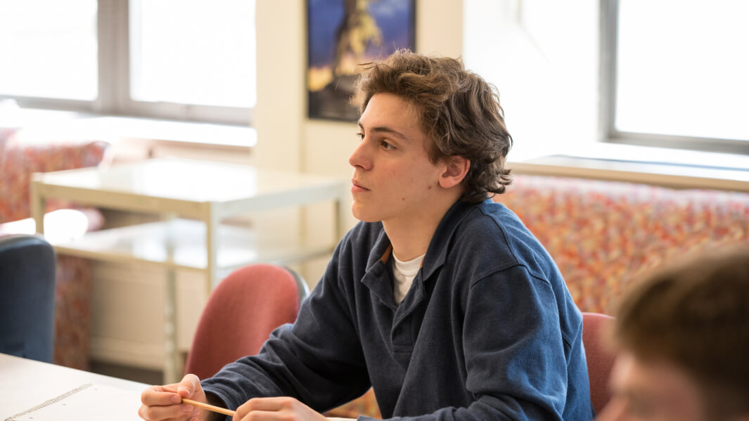 A student sits at a desk holding a pencil.