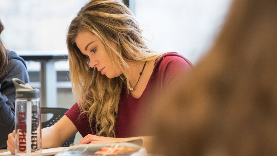 A student writes in a notebook at their desk.