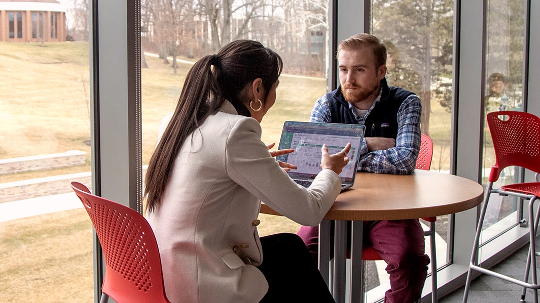 Two students collaborate at a table near a window.