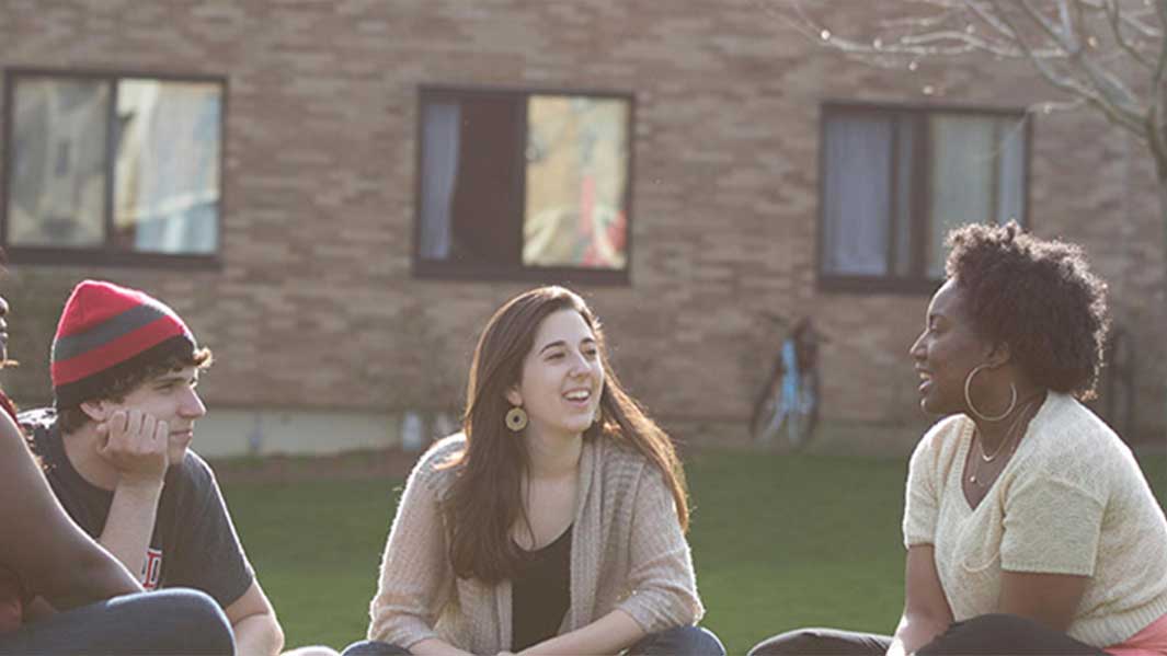 A group of students sit on the grass outside having a conversation.