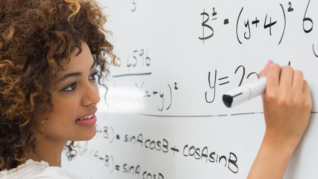 A student writes an equation with expo marker on a white board.