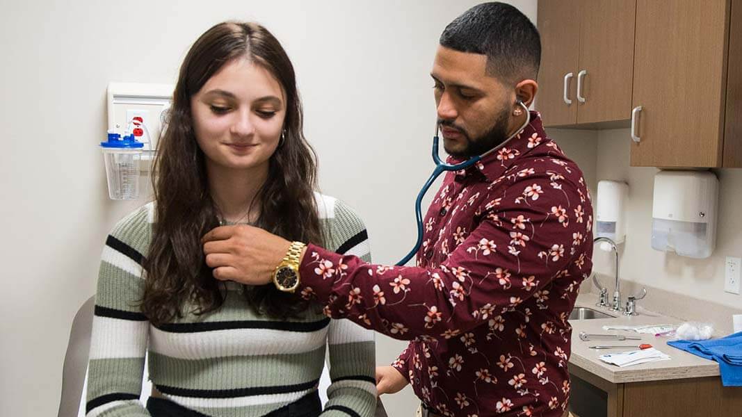 A man uses a stethoscope on a female patient.