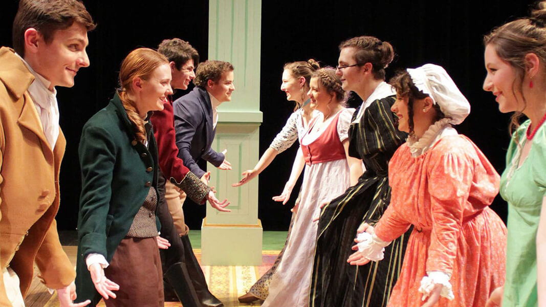 Theatre students performing on stage while dressed in early 19th century costumes.