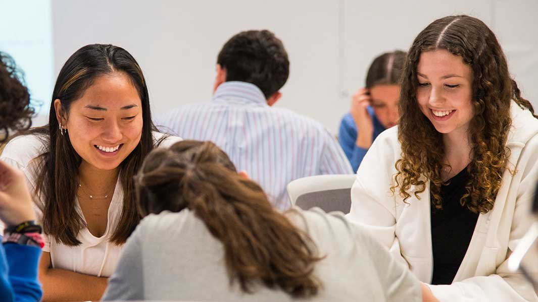 Actuarial science students smiling and gathered around a table collaborating