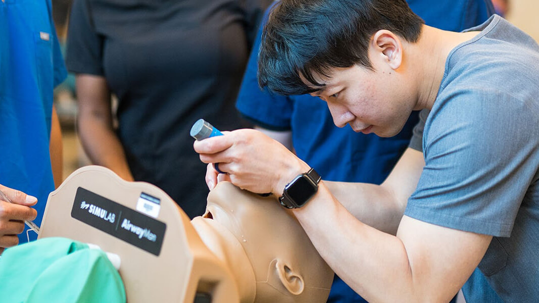 A student performs a medical exam on the nose of a manikin.