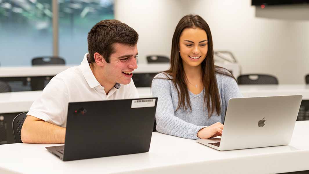 Two students sit at a table in a meeting room.