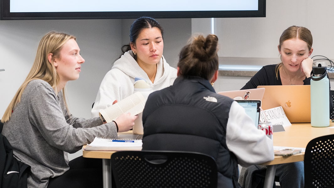 Four students sit and work collaboratively at a study room table.