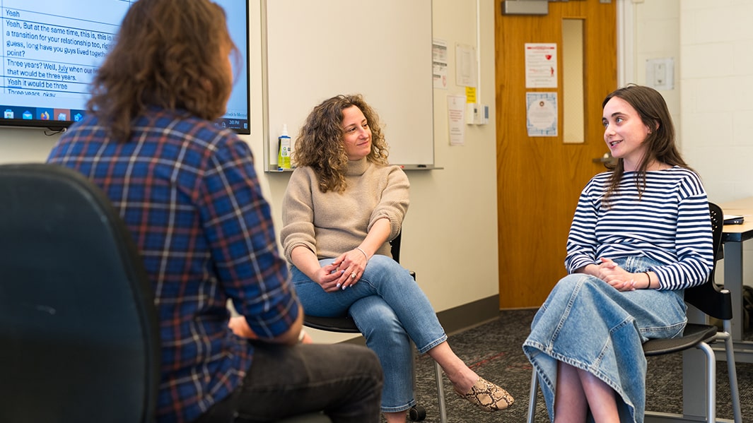 Two students sit across from a third as they engage in conversation with one another.