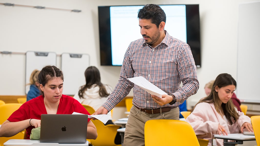 A professor points to a whiteboard.