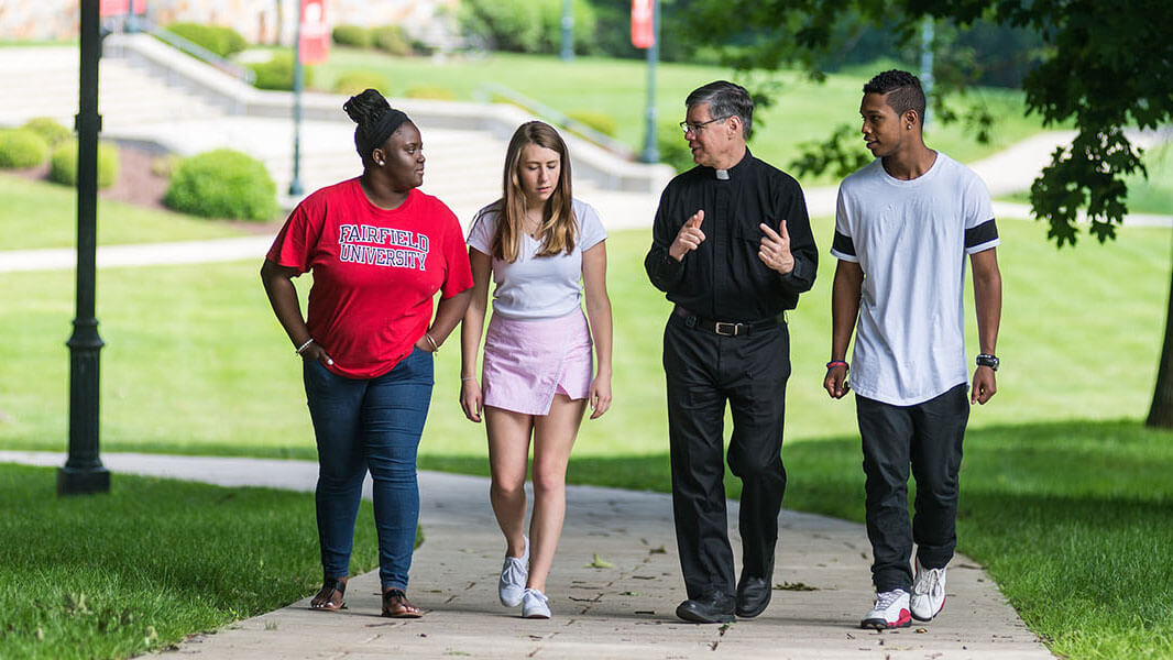 Three students walk with a Father on a stone path outdoors.