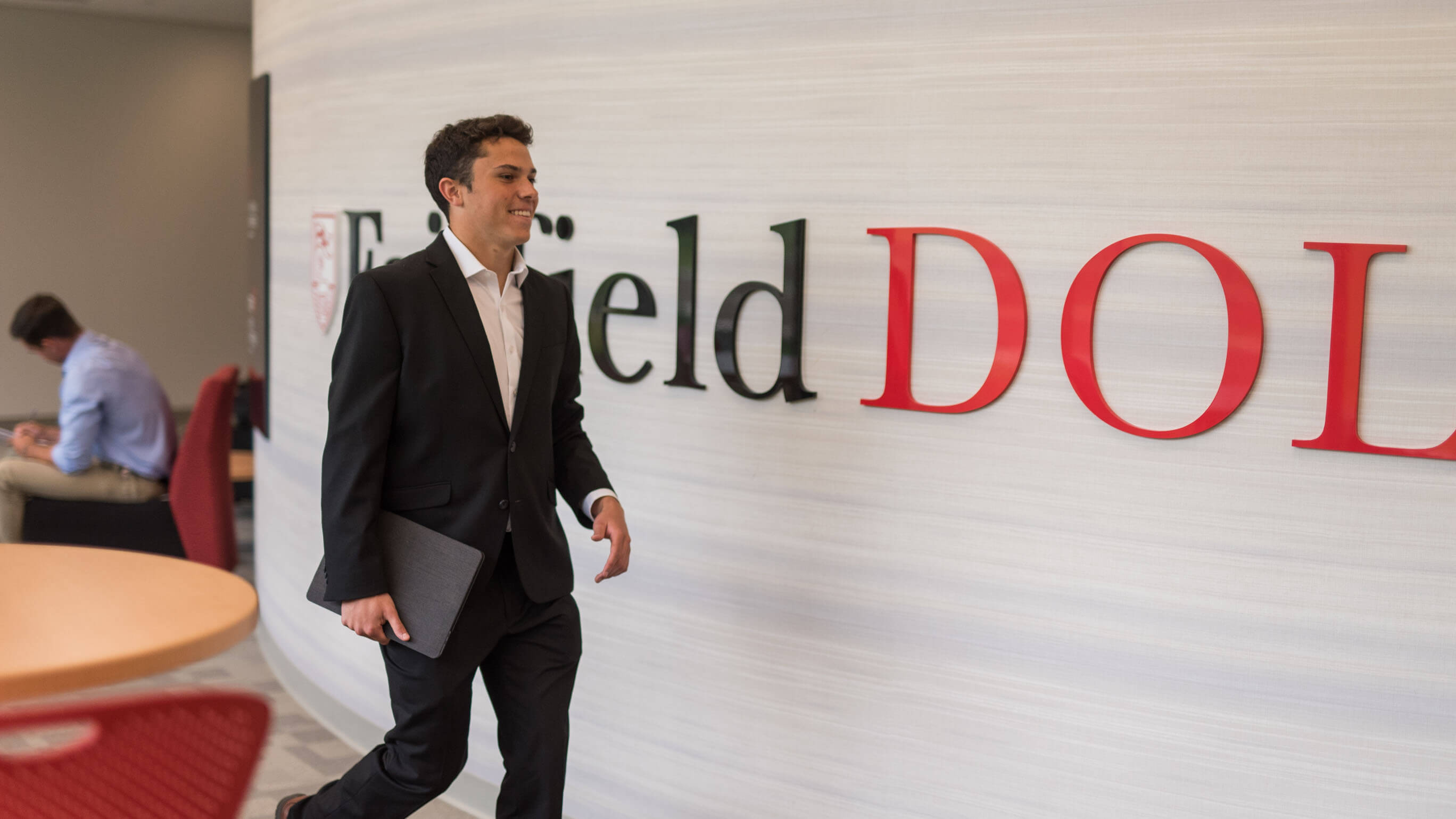 Student formally dressed walks past dolan sign inside of business school.