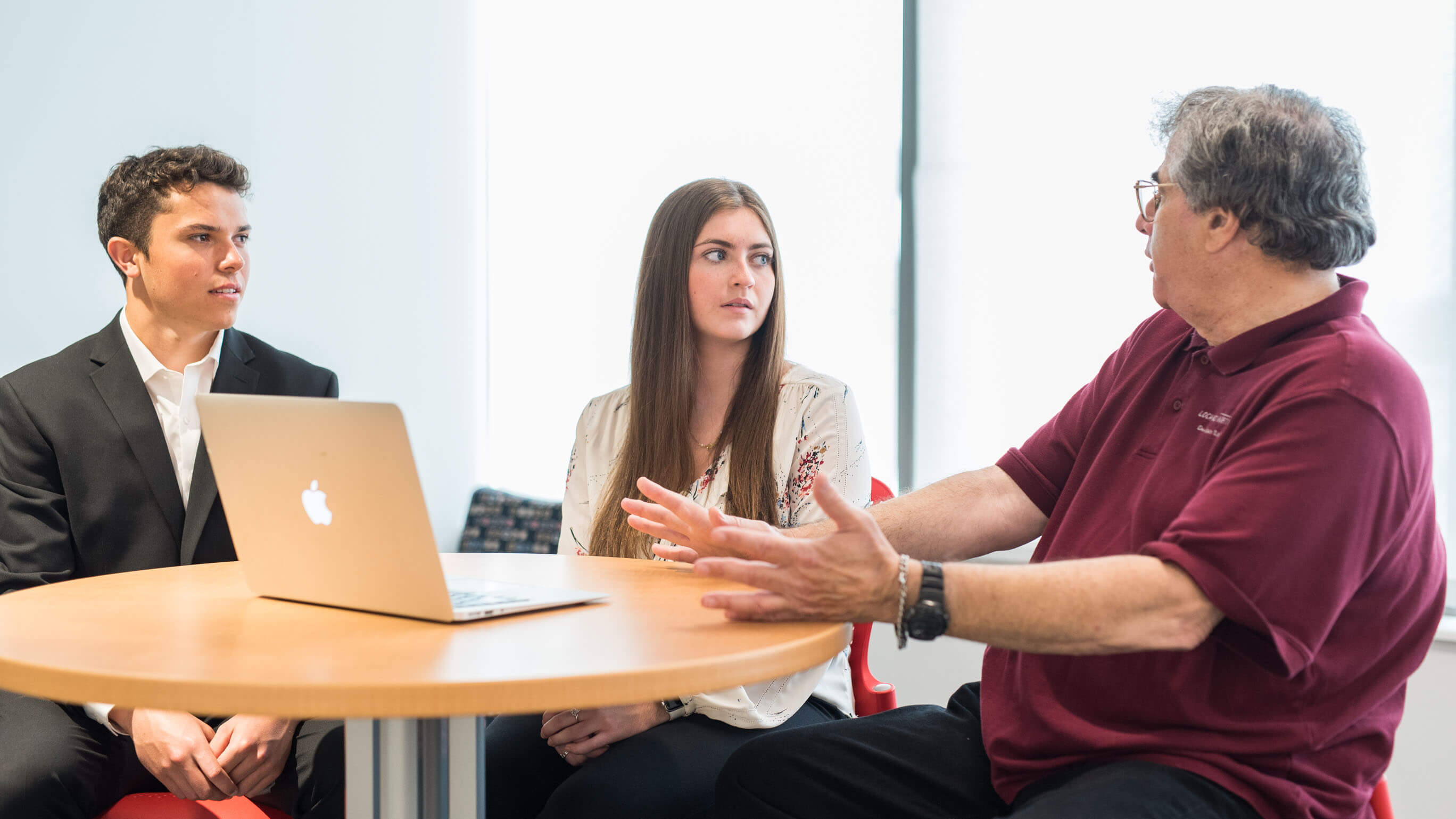 Two students sitting with a professor at a table.