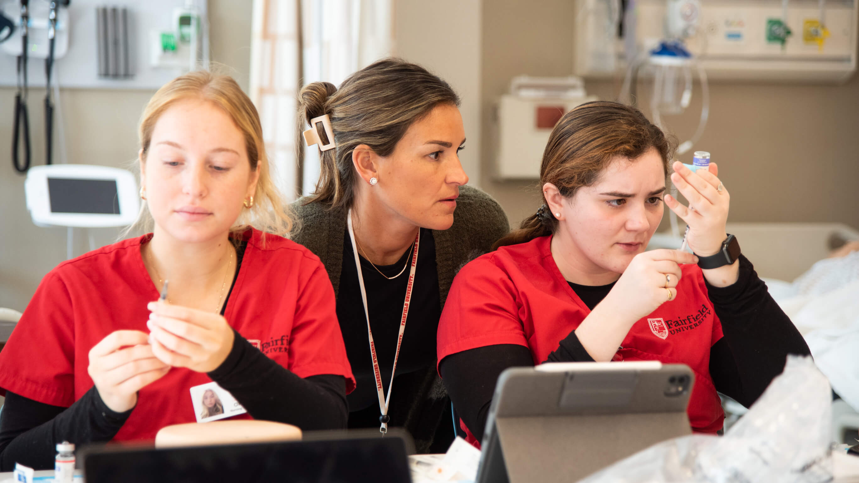 2 students in red scrubs sit in front of a professor.