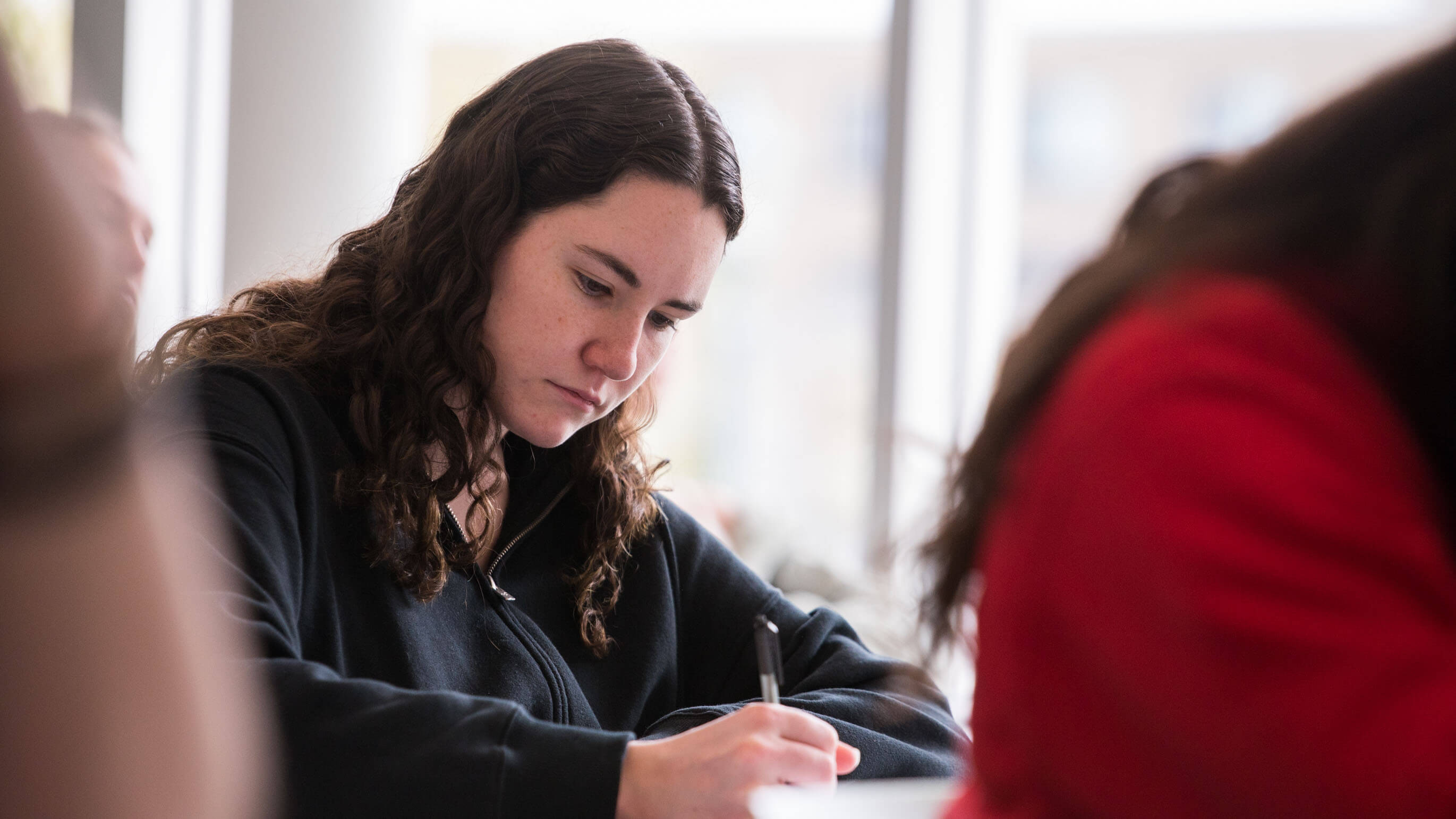 A student writes with a black pen on a piece of paper.