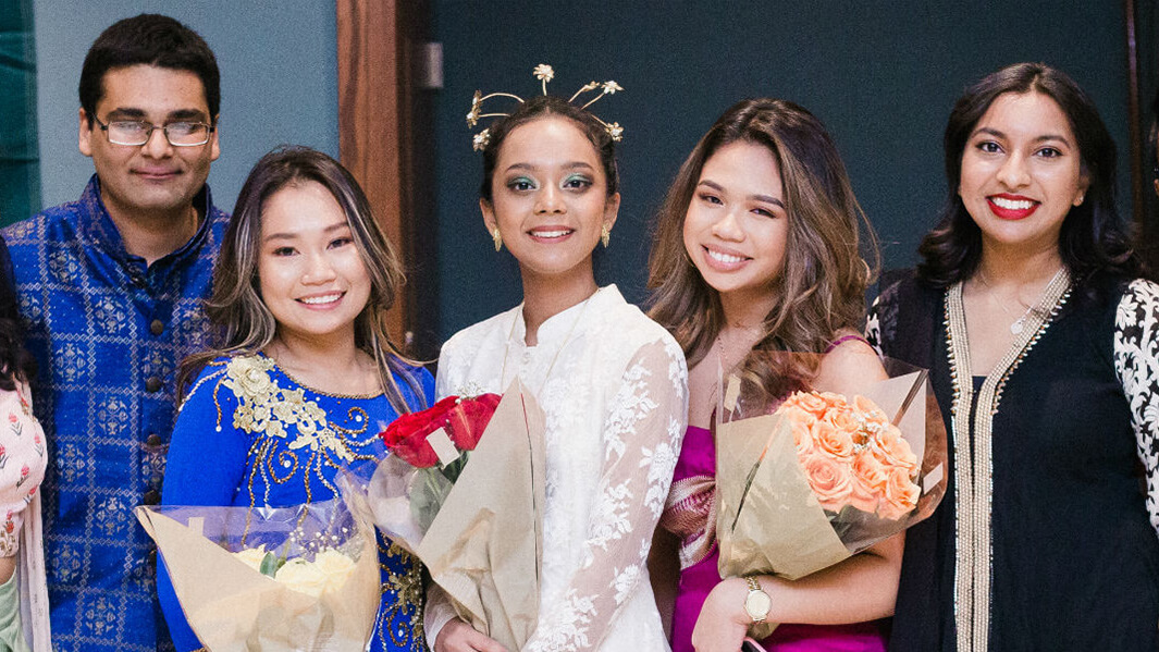 Asian Studies students smiling and standing seven in a row with the three of them in the middle holding flowers. 