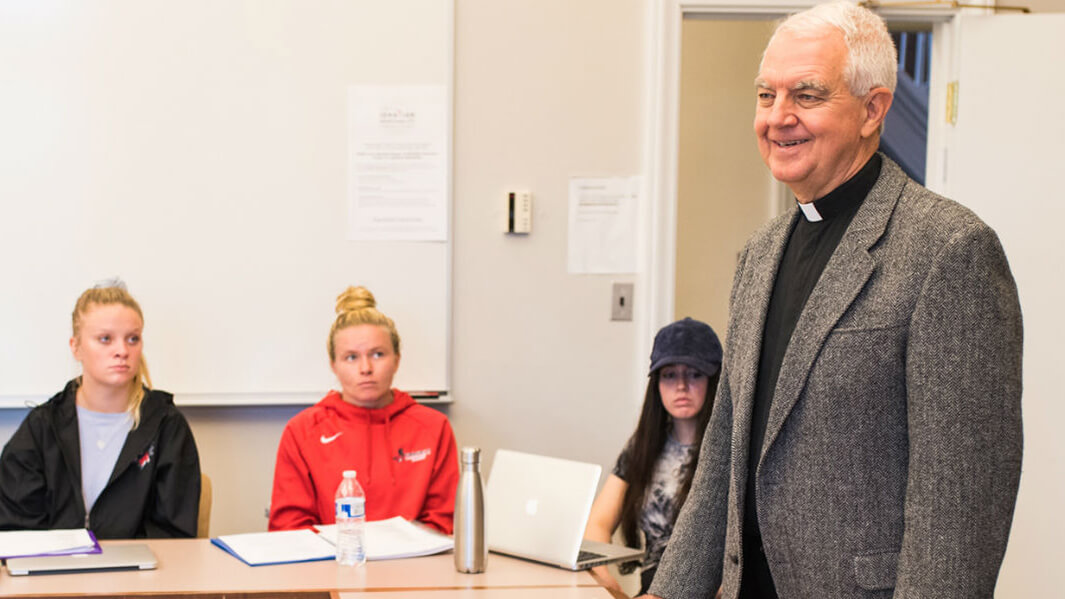 Priest giving a lecture in a small classroom.