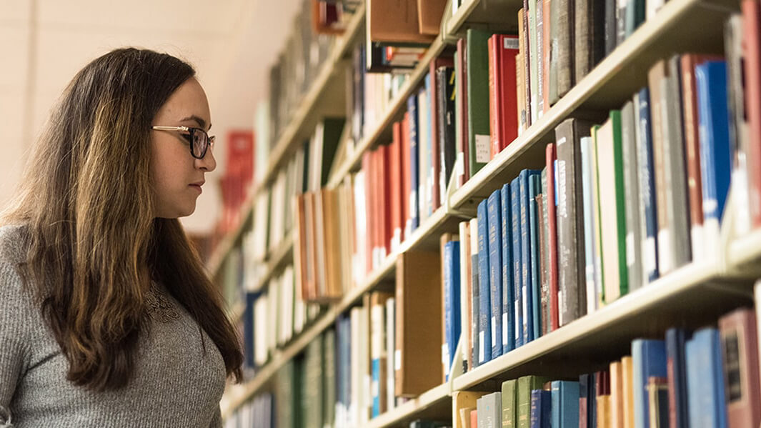 Student looking at a bookshelf in the library. 