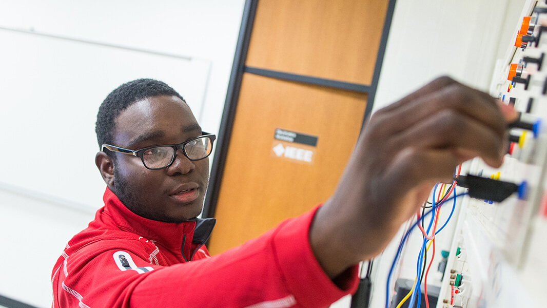 Side profile of an engineering student inserting cables into a machine on the wall. 