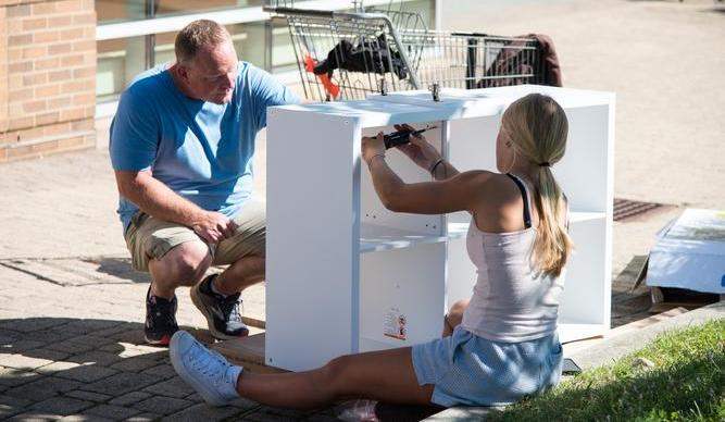 A student screws together a white shelving unit with help from her dad.