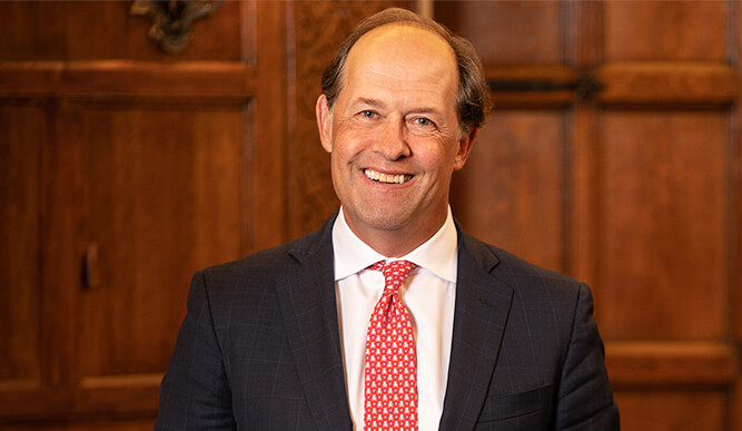 Photo of President Mark R. Nemec, PhD standing in front of a dark wooden background.