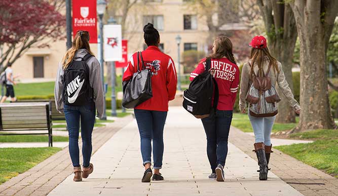 Four student walking down a path towards a residence hall.