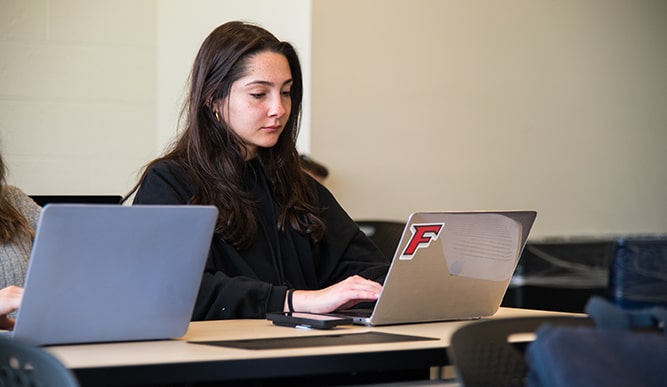 A student sits at a desk on her laptop with a Fairfield “F” sticker on the case.