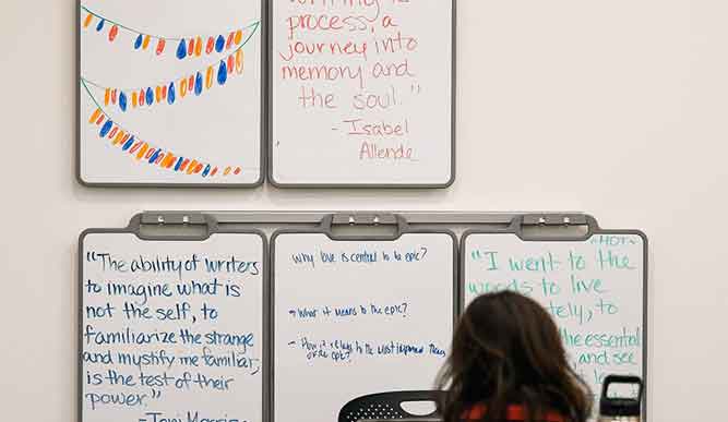 A person sits in front of five whiteboards that display various literary quotes.