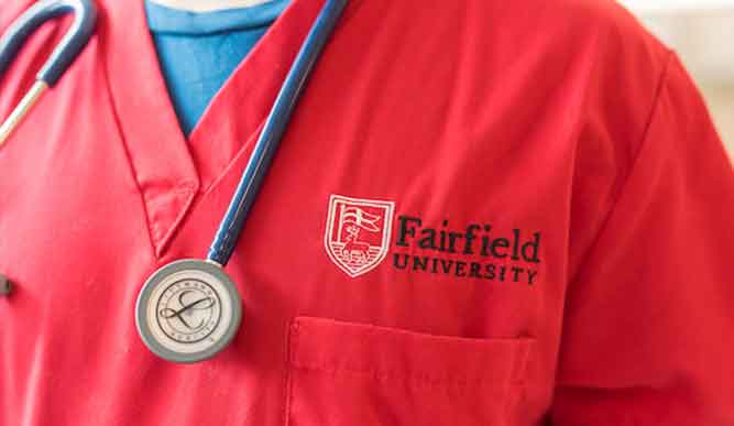 Closeup of a student in red scrubs with “Fairfield University” embroidered. 