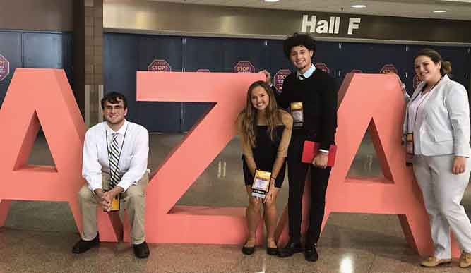 Students posing around large orange AZA sign. 