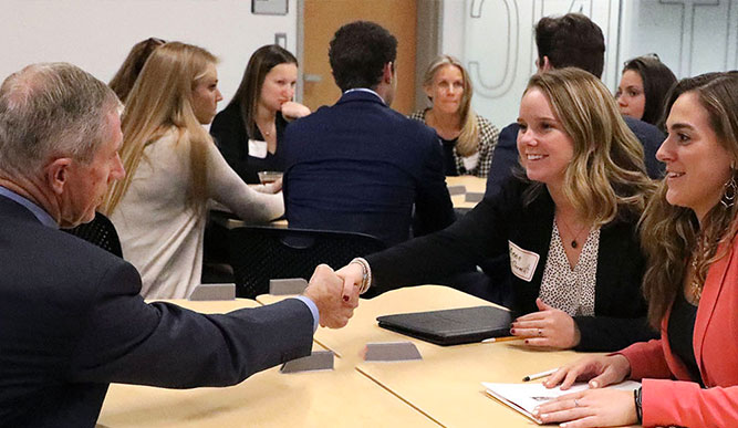 A group of people at a table, smiling and shaking hands in a friendly meeting atmosphere.