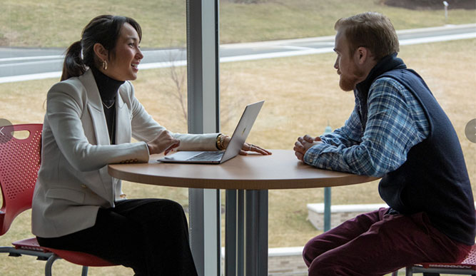 Two students wearing formal attire sit and collaborate in university space.