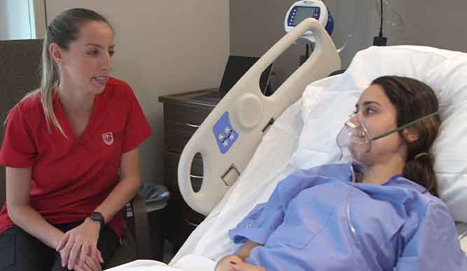 A woman lying in a hospital bed, wearing an oxygen mask, appears to be receiving medical care.