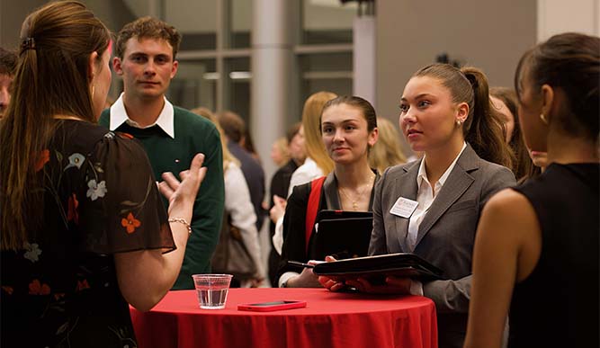 Student wearing formal attire standing around a table talking at an event. 