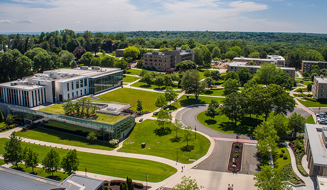 Overhead perspective of Fairfield University campus, highlighting green trees and architectural structures, illustrating a serene academic setting.