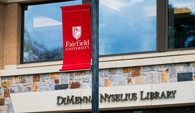 A ýƵƹۿ banner hangs off a lamp post in front of a building with a sign that reads “DiMenna-Nyselius Library”. 