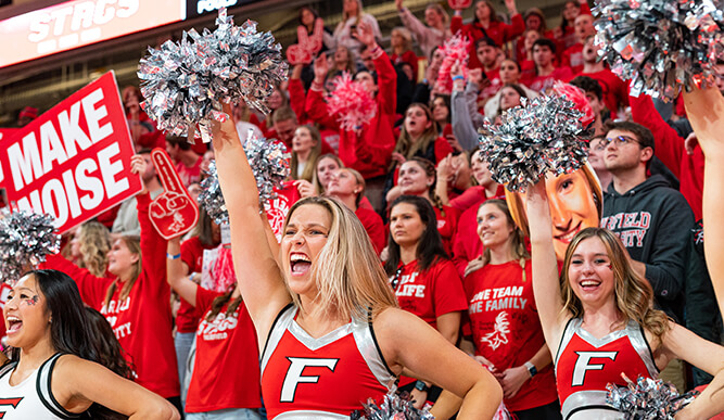 Cheerleaders stand in front of a crowd at a sports game.