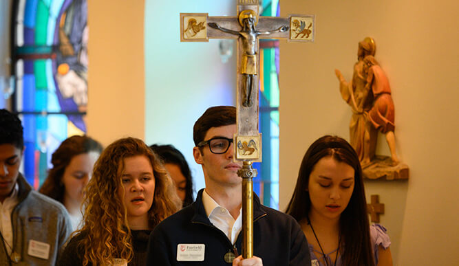 Students processing down a church aisle with a crucifix.