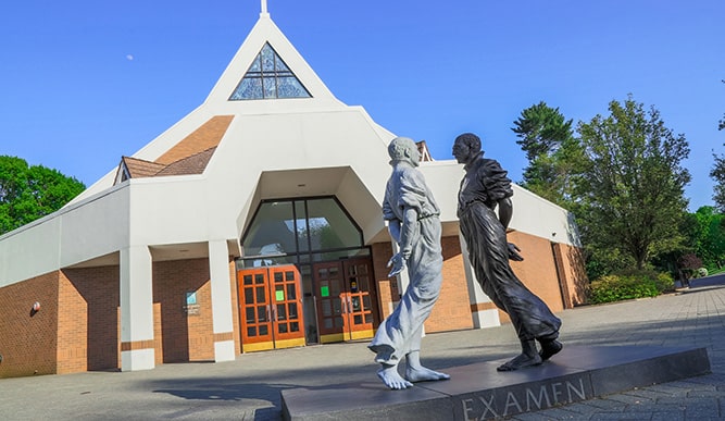 Sculpture of Saint Ignatius staring at another darker sculpture of Saint Ignatius in front of Fairfield’s chapel on campus.