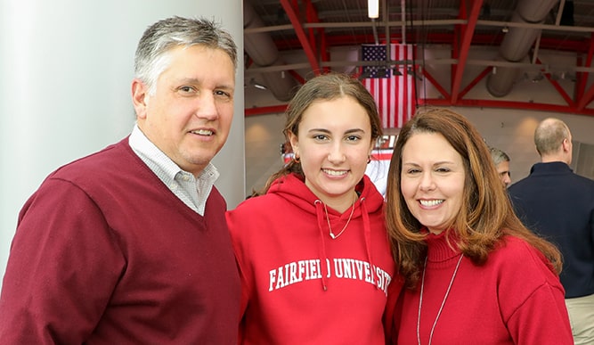 A student smiles between their parents.