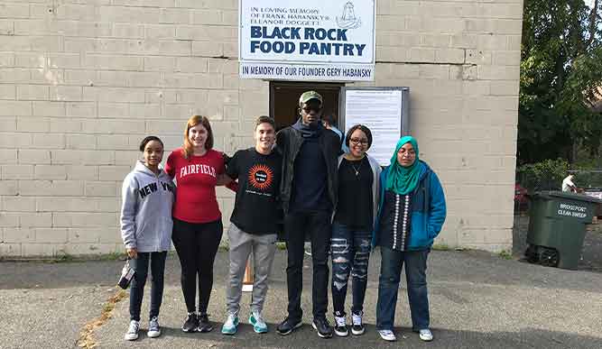 A group of students stands in front of a sign that reads “Black Rock Food Pantry”.